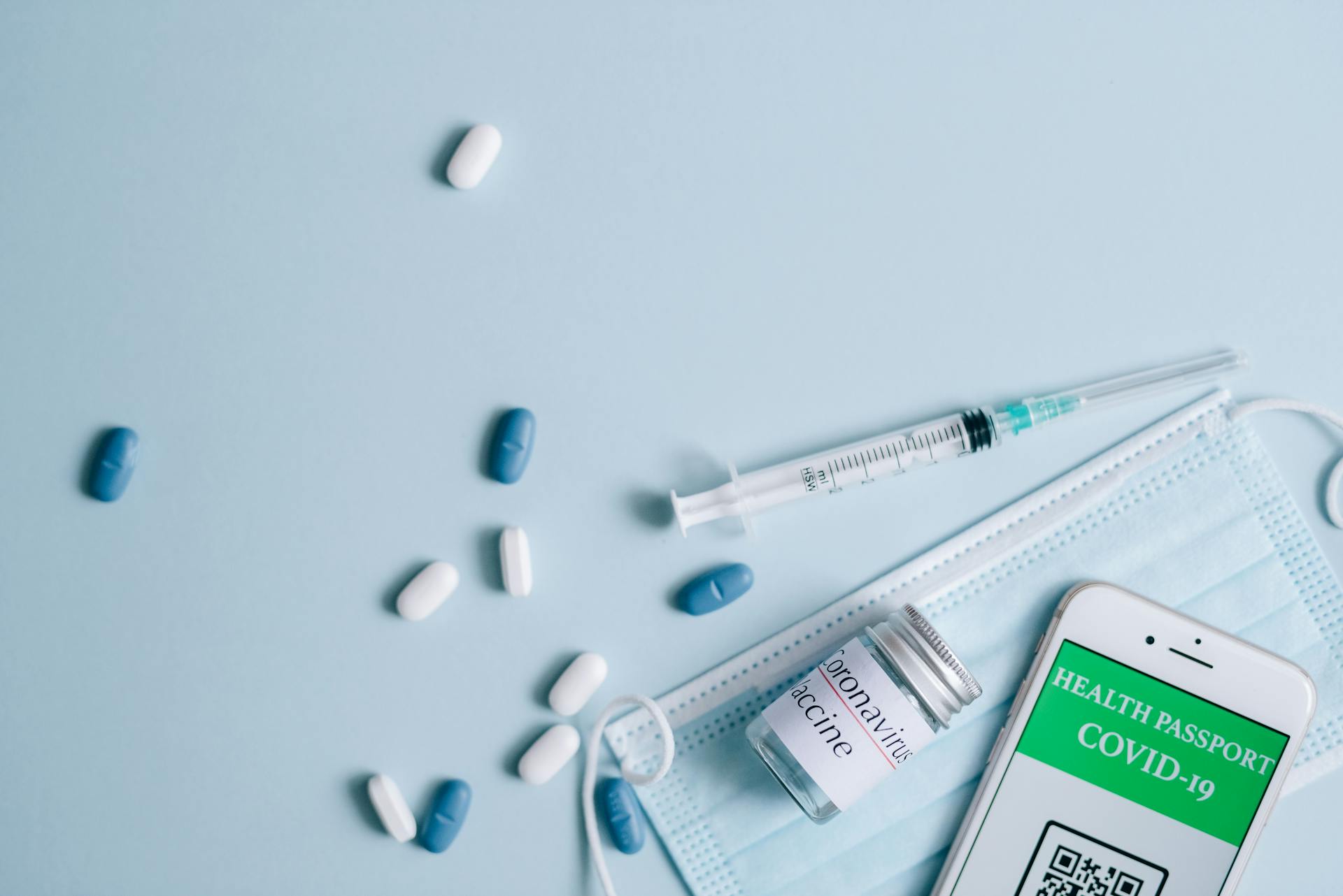 Top View of a Surgical Mask, Medication and a Smartphone Displaying a Covid-19 Health Passport