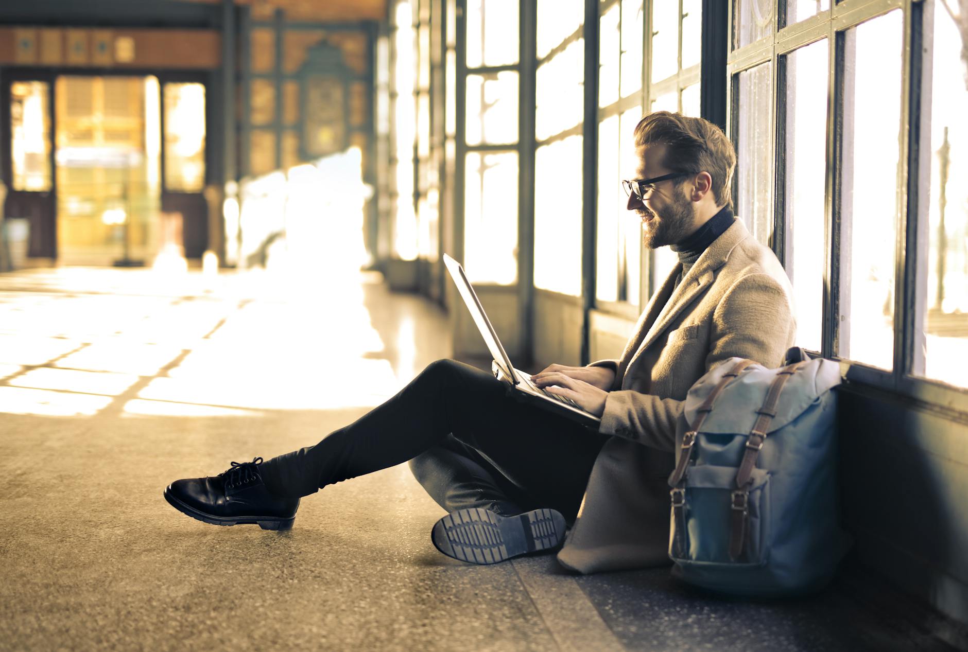 A young businessman sitting in a corridor typing on laptop