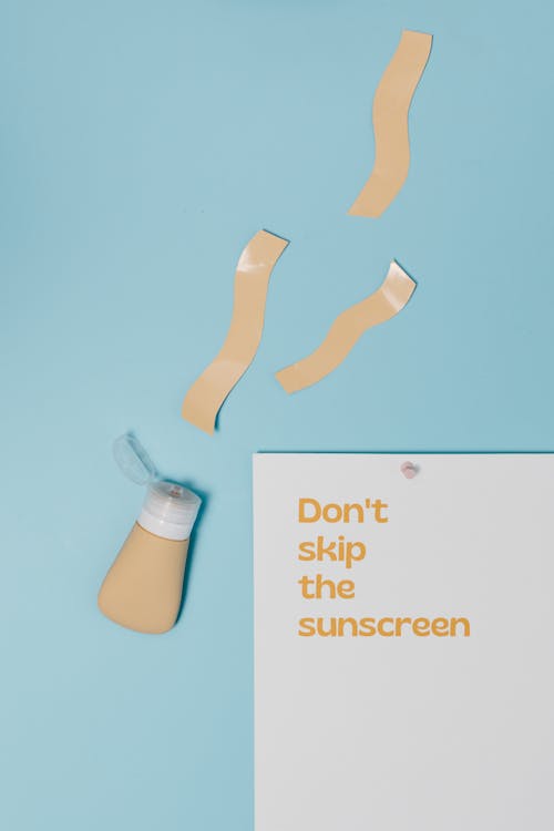 Free Paper with a Text Saying "Dont Skin the Sunscreen" Lying on Blue Background Stock Photo