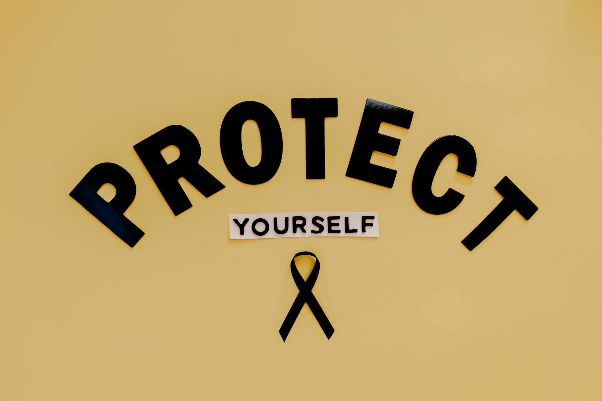 Text Saying "Protect Yourself" and a Skin Cancer Symbol - Black Ribbon - Lying on Brown Background