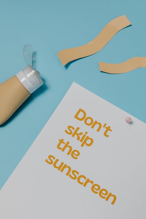 Free Paper with a Text Saying "Dont Skin the Sunscreen" Lying on Blue Background Stock Photo