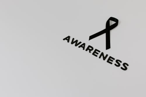 Black Ribbon Symbolizing Skin Cancer and a Sign Saying "Awarness" Lying on White Background