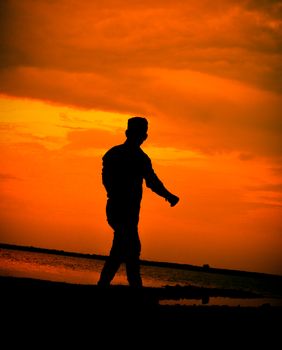 Silhouette of a person walking on the beach with an orange sunset background.