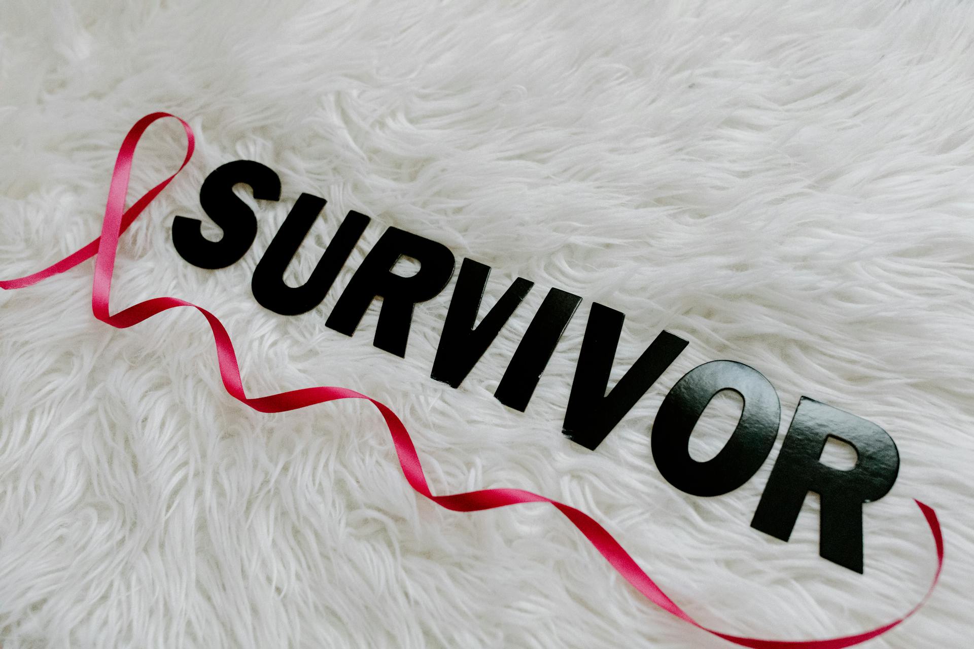 Text Saying "Survivor" an a Pink Ribbon Symbolizing Breast Cancer Lying on White Background