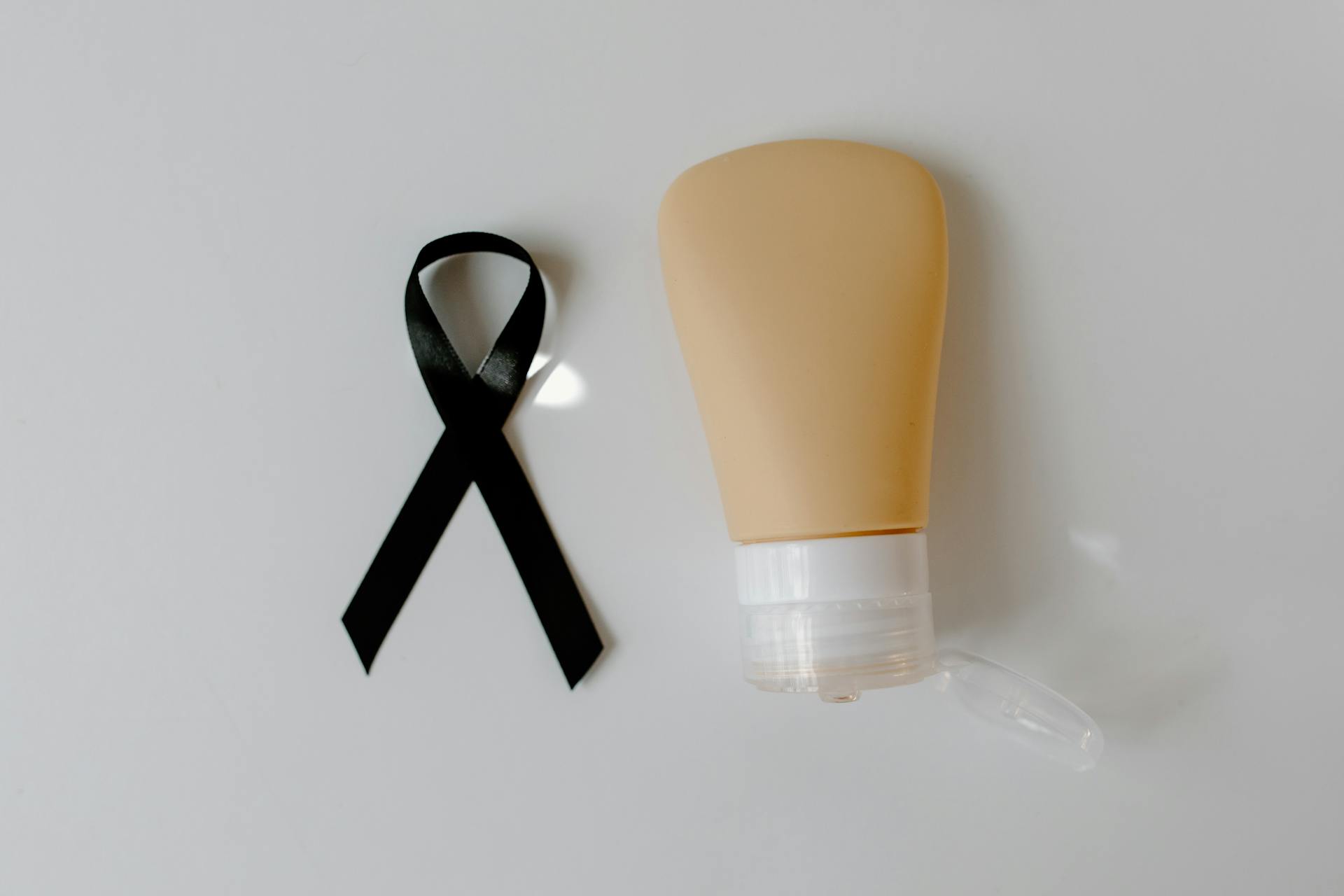 Black Ribbon Beside a Plastic Tube on a White Surface