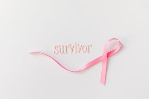 Pink Ribbon Beside Letters on a White Surface