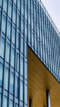 Vertical shot of a modern glass building with geometric architecture and reflective windows.