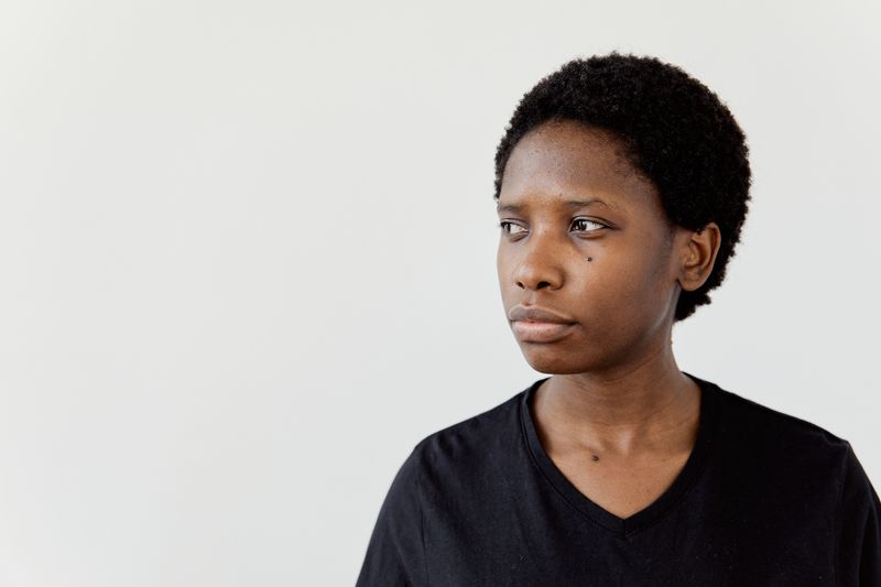 Portrait of a Black woman with short natural hair in a black t-shirt, looking to the side against a plain white background, used to illustrate a guide to alopecia areata in Black women.