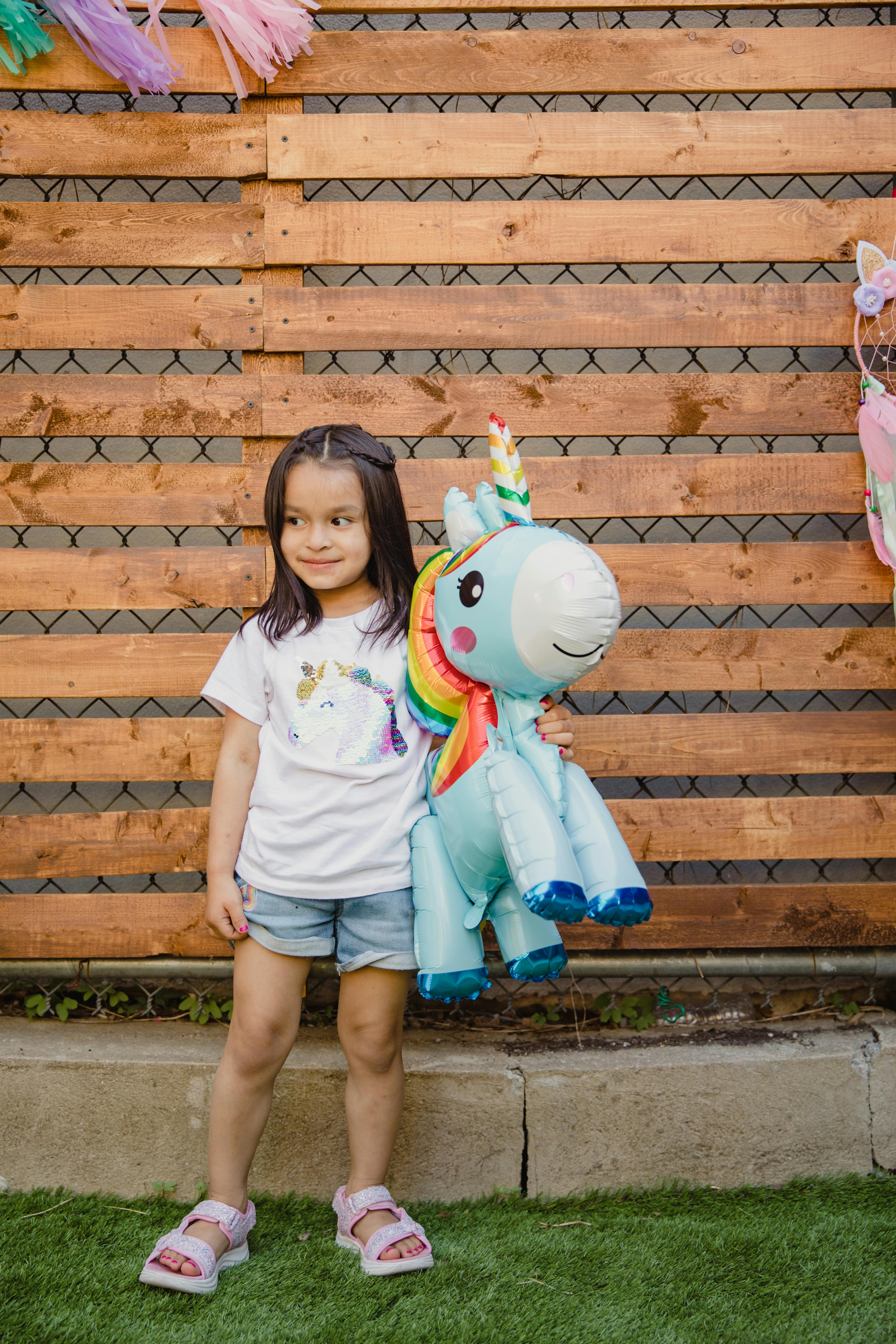 A young girl joyfully holds a vibrant unicorn inflatable outdoors.
