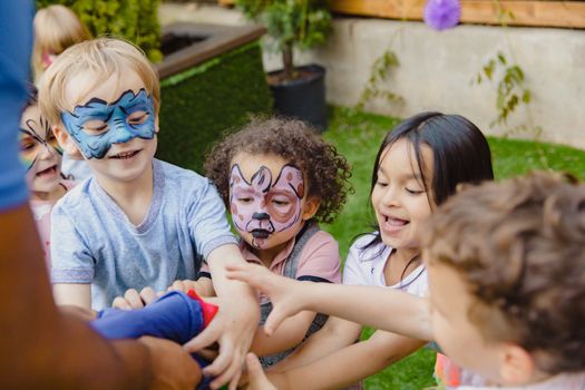 Group of children with face paint enjoying playtime outdoors, laughing and engaging in games.