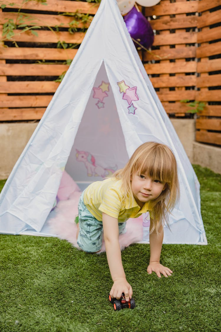 A Boy Sitting Near The Tent On The Green Grass