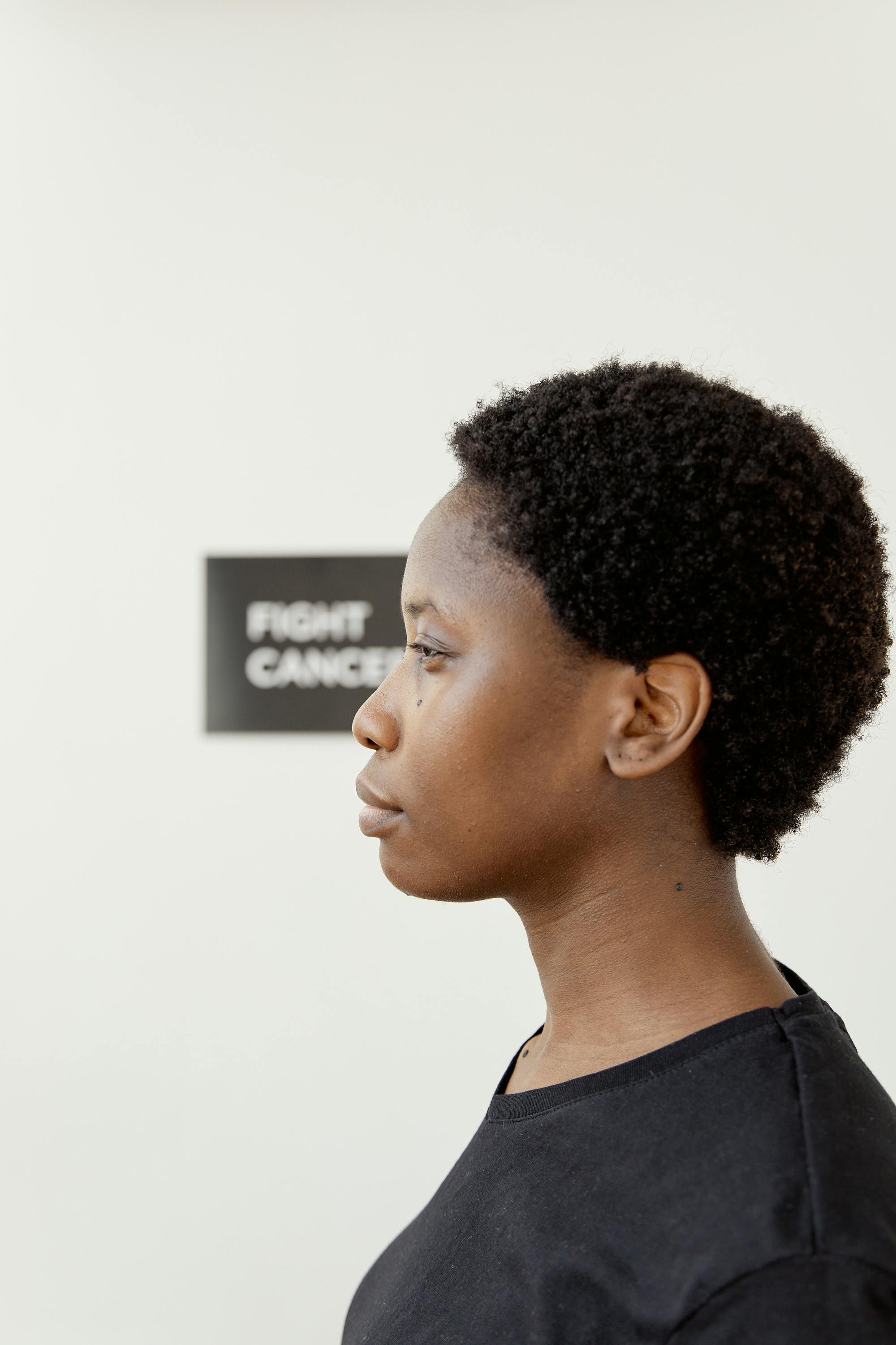 Profile portrait of a woman with afro hair in a black t-shirt supporting cancer awareness with a conceptual message.