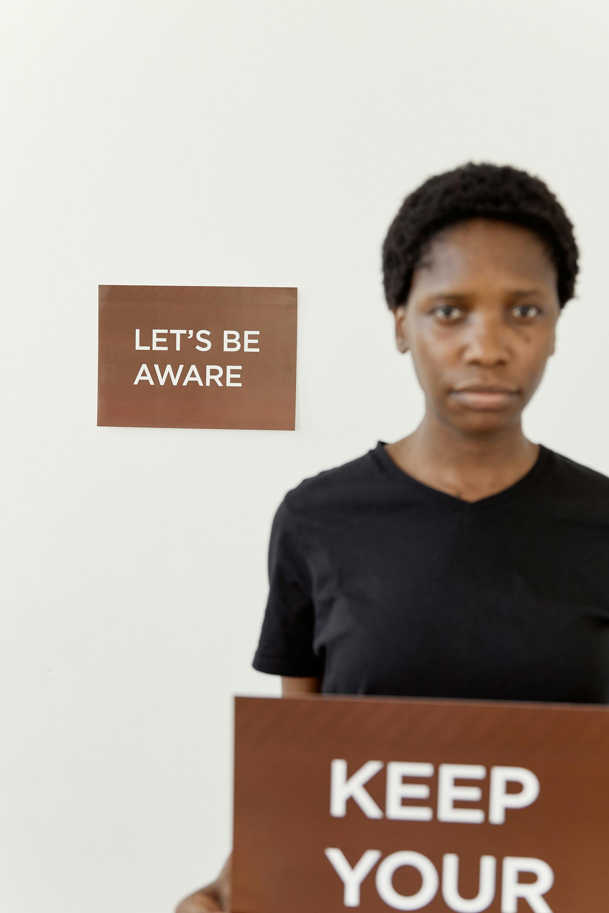 African American woman holding awareness sign indoors. Let's be aware message.