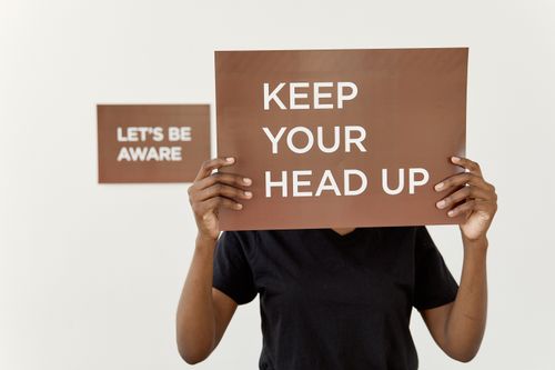 Free A motivational sign reading 'KEEP YOUR HEAD UP' held by a person indoors. Stock Photo
