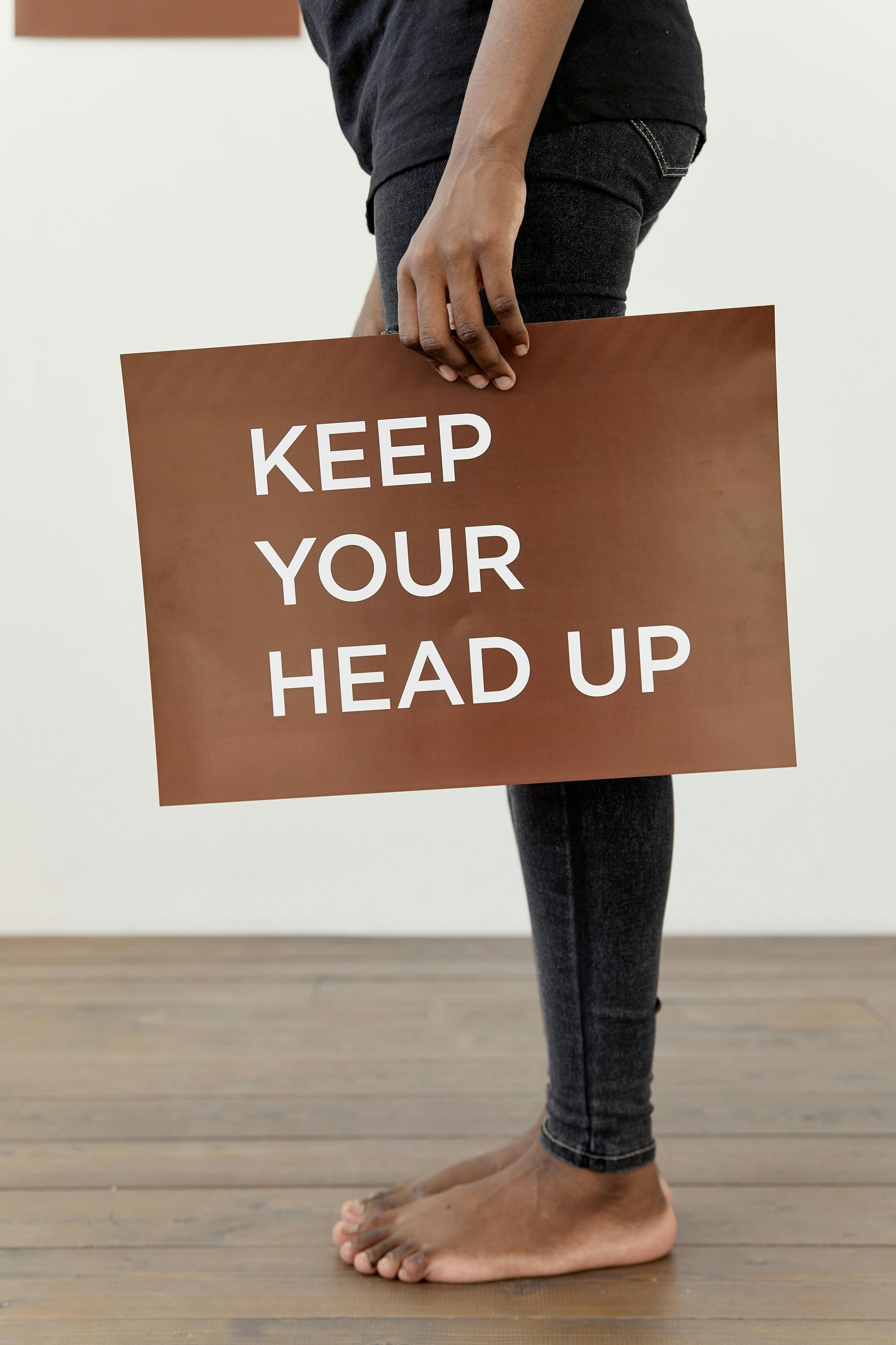 A motivational message 'Keep Your Head Up' on a sign held by a standing figure.