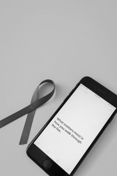 Black smartphone with motivational text and gray awareness ribbon, symbolizing strength.