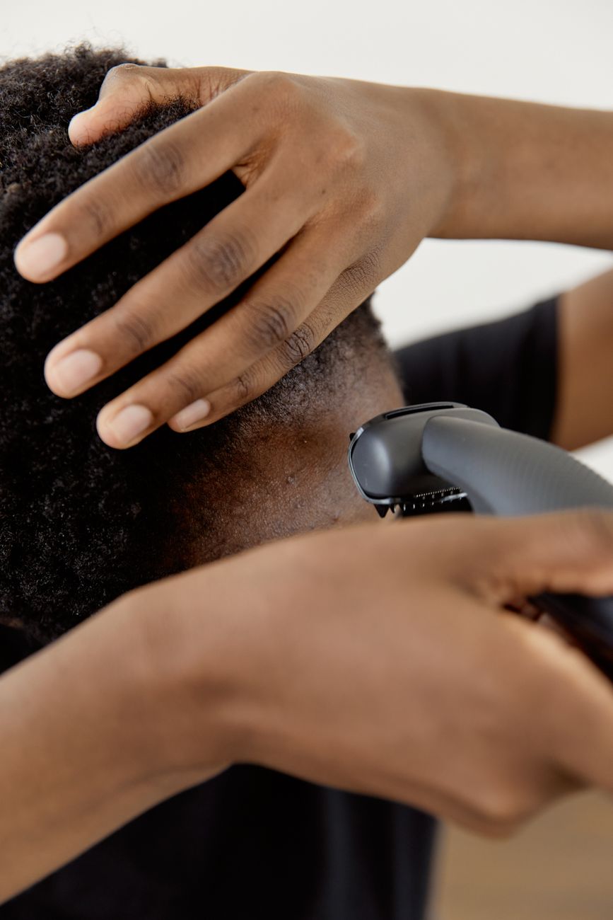 A close-up shot of a person using an electric razor to shave their head, focusing on the hands and hair.