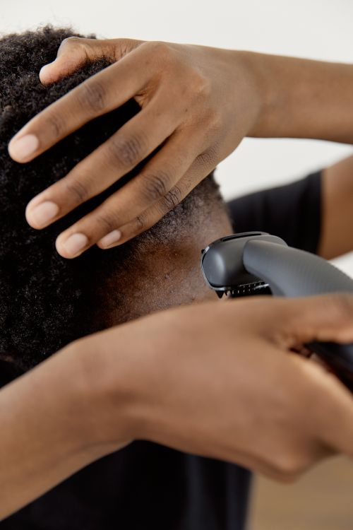 Free A close-up shot of a person using an electric razor to shave their head, focusing on the hands and hair. Stock Photo