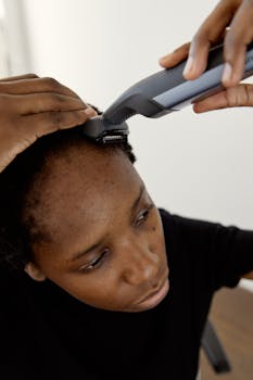 Close-up of an African woman using a hair clipper to shave her head indoors.