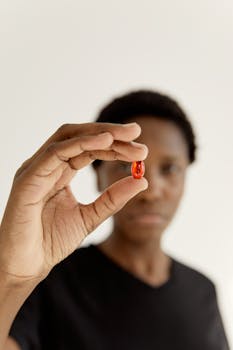 Close-up of a person holding a red pill against a white background, emphasizing health and medicine.