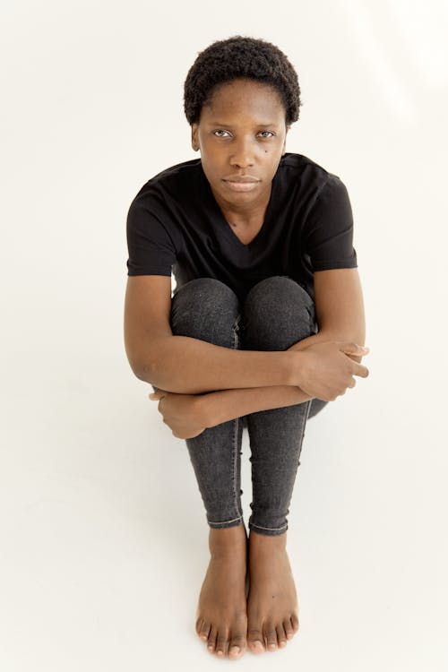 Afro-Haired Woman in Black Shirt Looking at Camera while Sitting on a White Surface