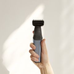 A hand holding a slim black trimmer against a pale wall