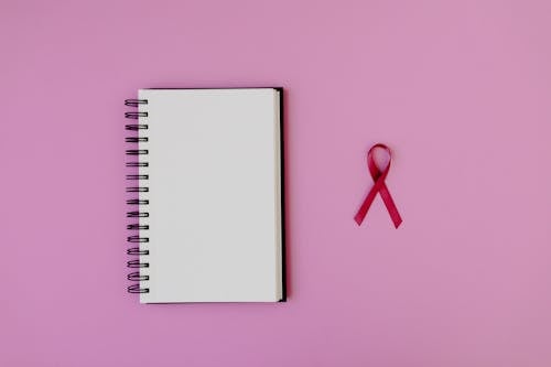 Free Pink ribbon and notebook on pink background symbolizing breast cancer awareness. Stock Photo