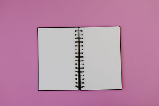 Flat lay of an open spiral notebook on a vibrant pink background, perfect for creativity.