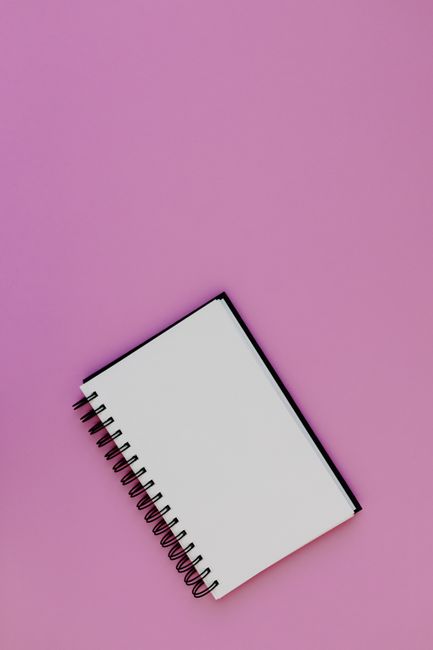 Fotomural Vista plana de un cuaderno espiral blanco sobre un fondo rosa vibrante.