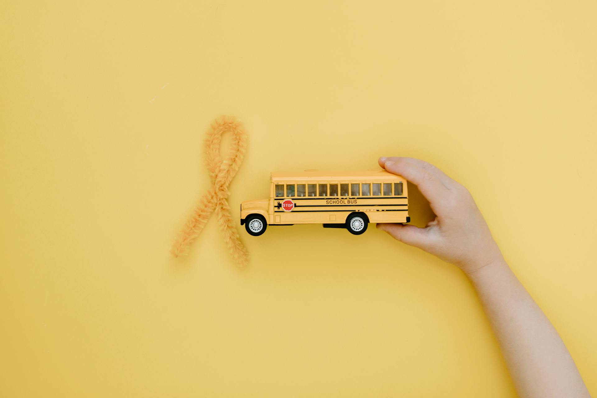 Child Holding a School Bus Toy next to a Yellow Ribbon Symbolizing Bone Cancer