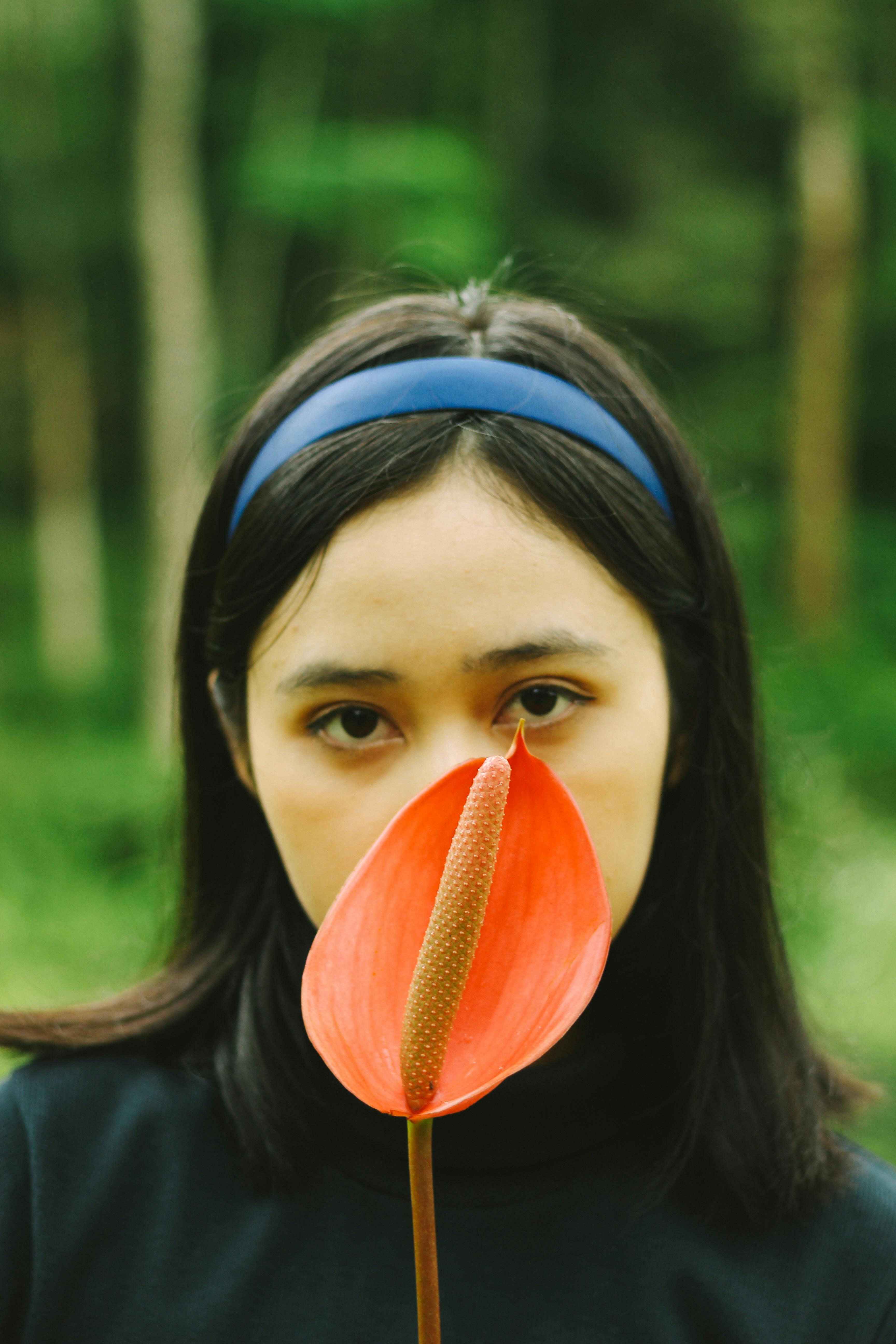 A woman holds an anthurium flower in front of her face outdoors.