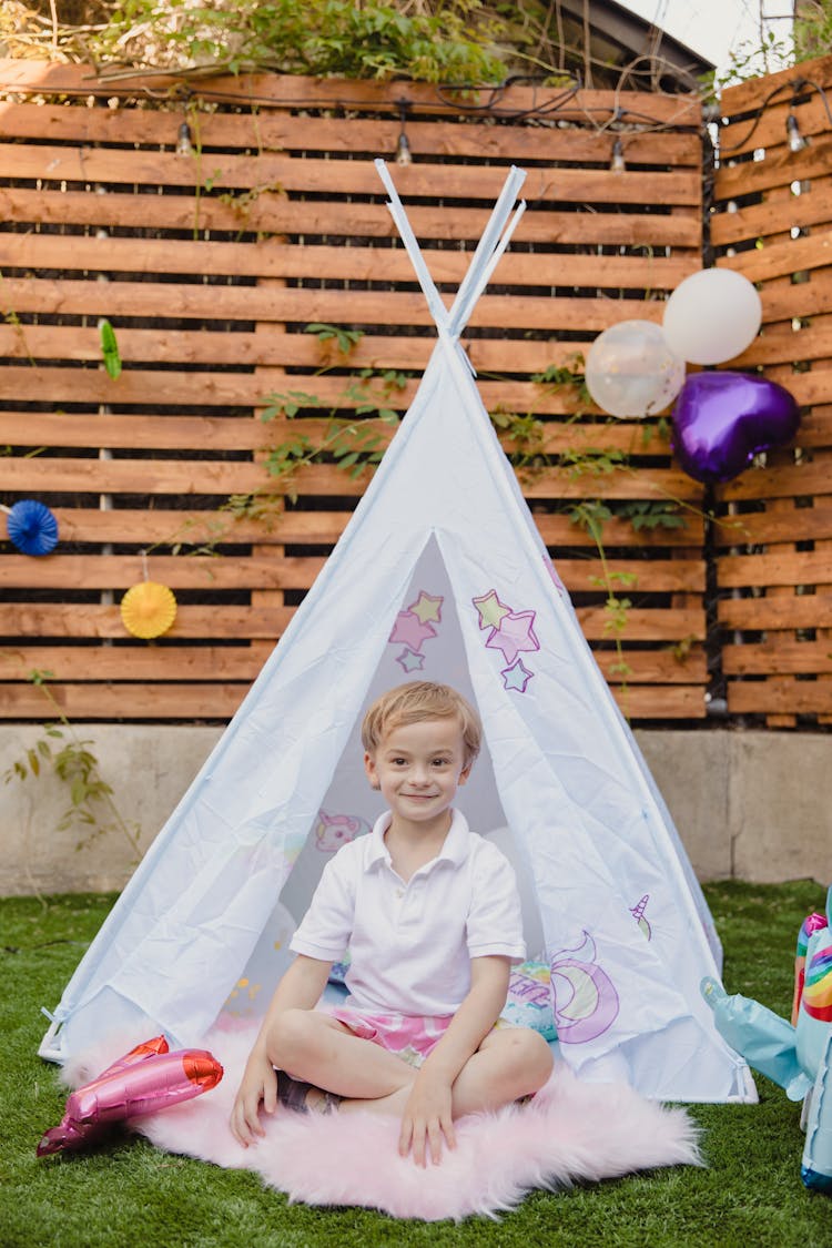 Kid In White Polo Shirt Sitting Beside A Teepee