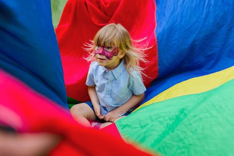 Little Child Sitting On A Colorful Parachute