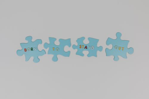 Free Blue puzzle pieces with the phrase 'Born to Stand Out' on a white background. Stock Photo