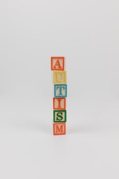 Vertical stack of colorful wooden blocks spelling 'AUTISM' on a white background.