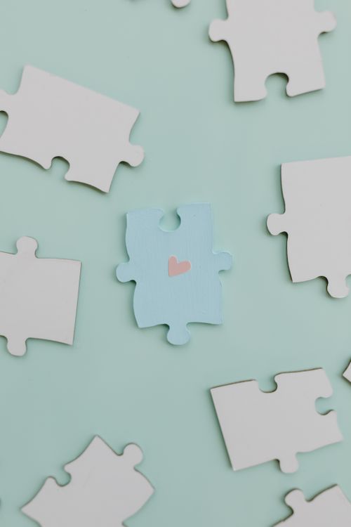 Free A collection of white and blue jigsaw puzzle pieces with a heart symbol on pastel green background. Stock Photo