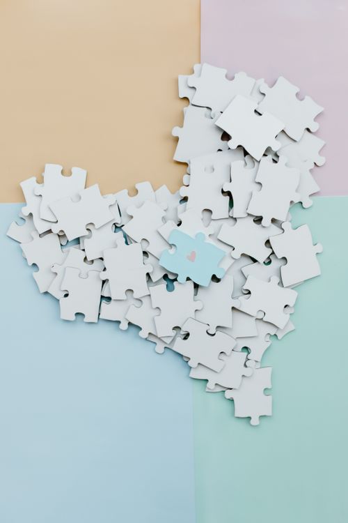 Free A collection of white puzzle pieces forming a heart shape on a soft pastel background. Stock Photo