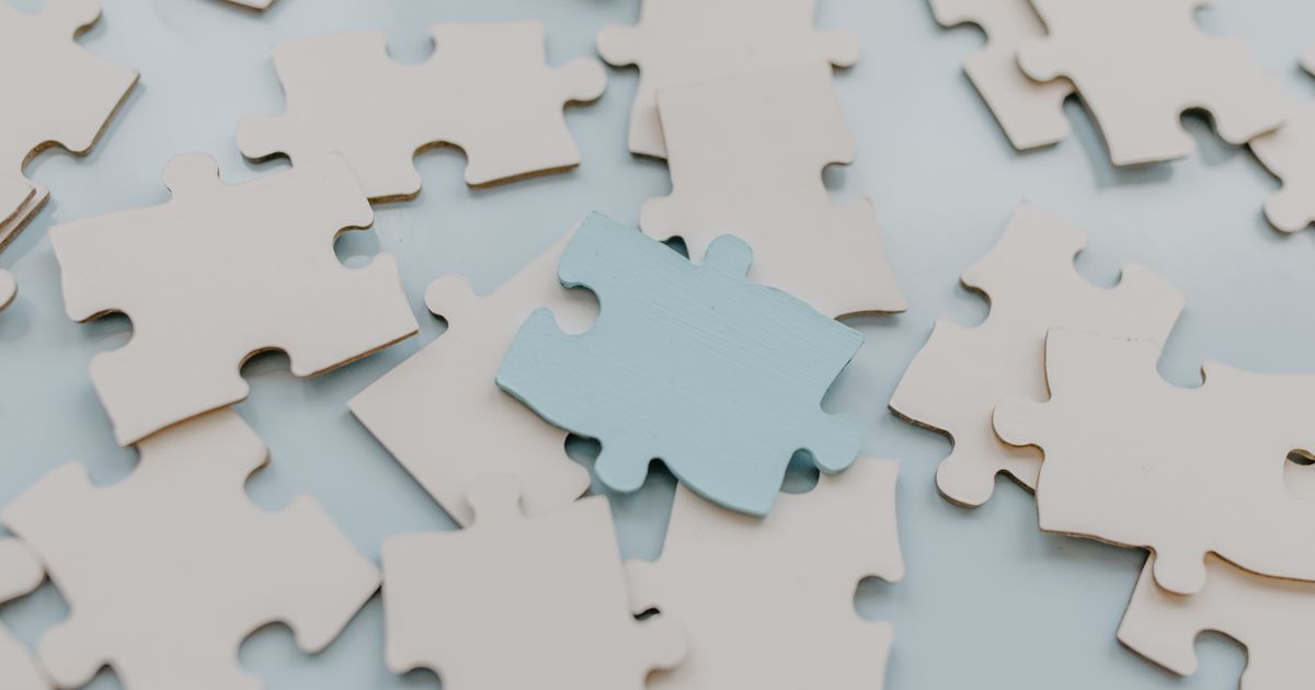 A close-up view of scattered puzzle pieces on a light background, featuring a unique blue piece.
