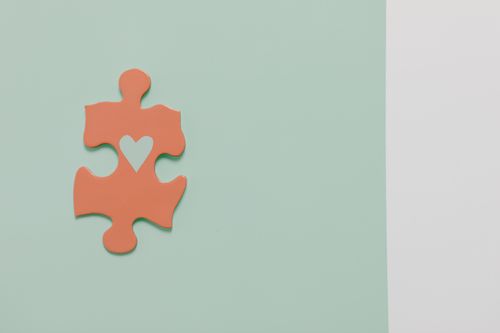 Free A single puzzle piece with a heart cutout on a pastel green and white background, showcasing minimalism. Stock Photo