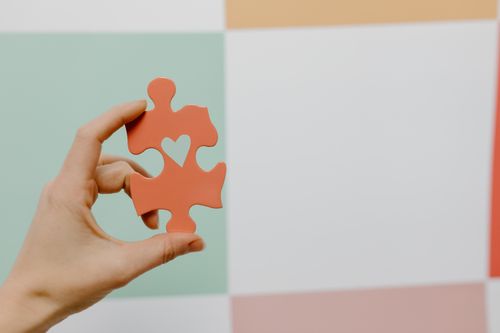 Free Close-up of a hand holding a heart-shaped puzzle piece against a colorful background. Stock Photo