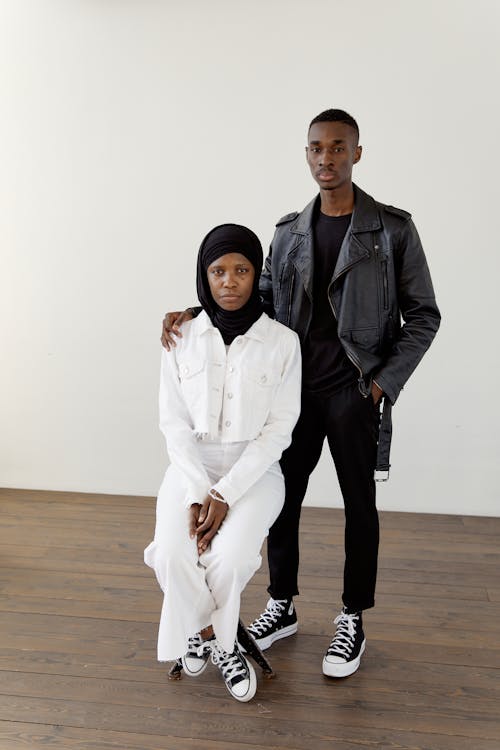 A Man in Black Leather Jacket Standing Near Her Partner Sitting on the Chair