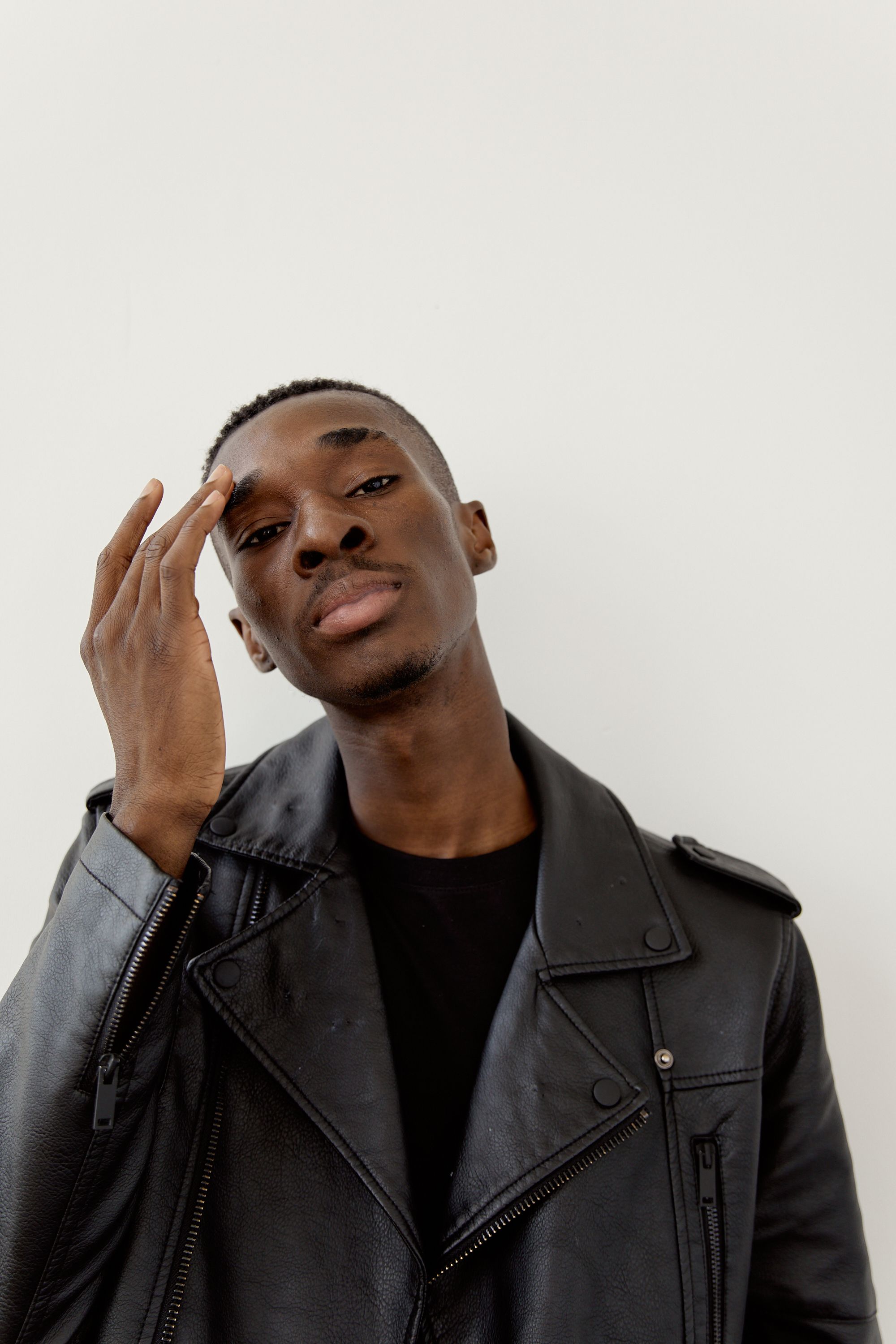 Portrait of a fashionable young man posing in a leather jacket against a white background.