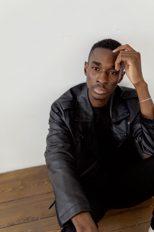 Free Man in a black leather jacket posing on a wooden floor with a contemplative expression. Stock Photo