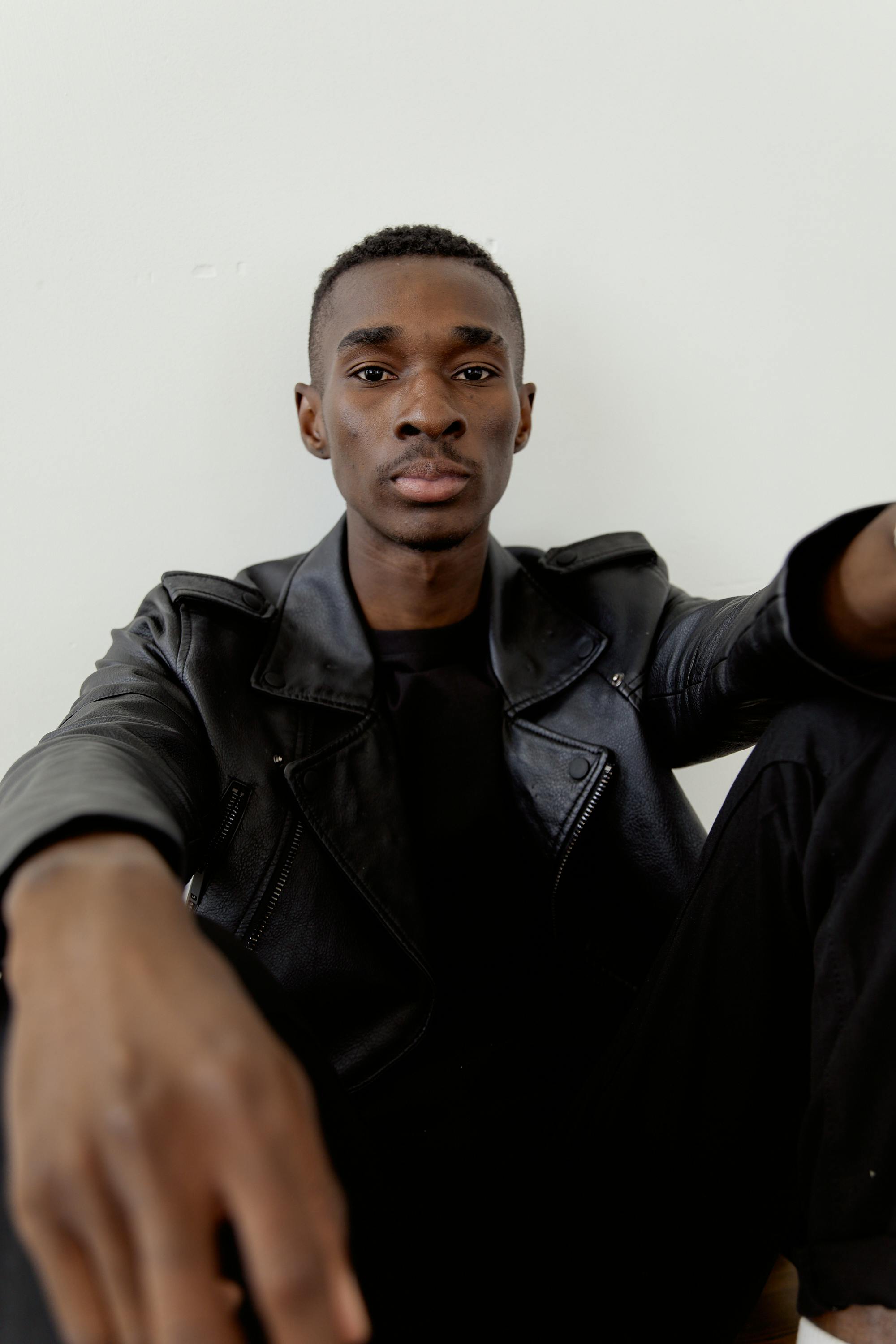 Young man posing confidently in a fashionable black leather jacket indoors.