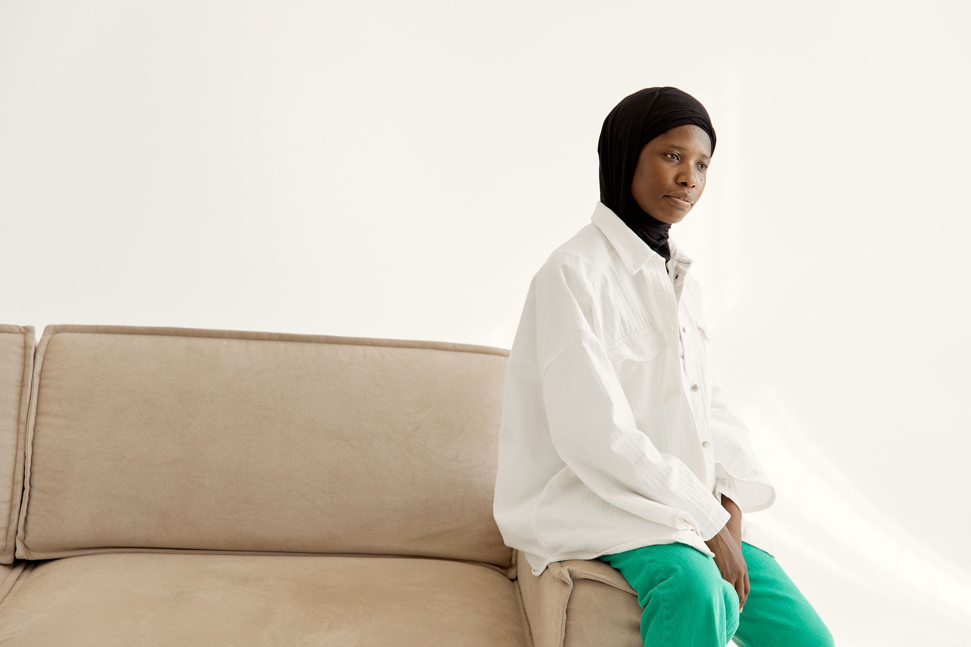 Elegant portrait of a woman wearing a hijab and white shirt, seated on a sofa.