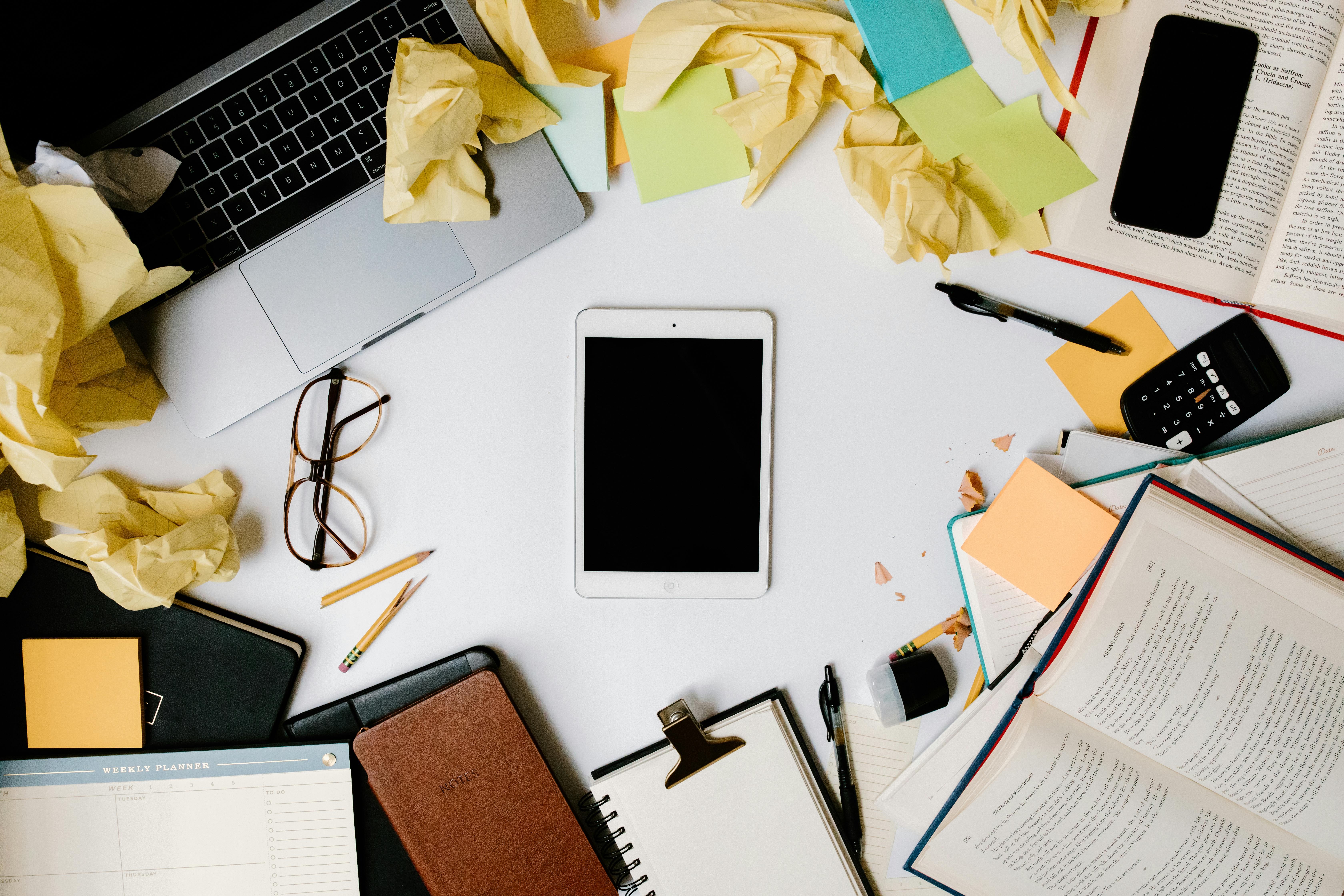 ipad surrounded with office supplies and crumpled papers