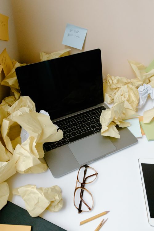 Free A messy desk covered with crumpled papers and a laptop reflecting disorganization. Stock Photo
