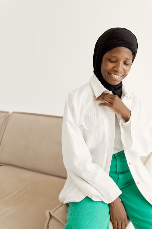Free Cheerful Muslim woman sitting on a couch, wearing a hijab and smiling warmly. Stock Photo