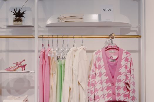 Stylish women's clothing on rack featuring pink cardigan and green dress inside a boutique.