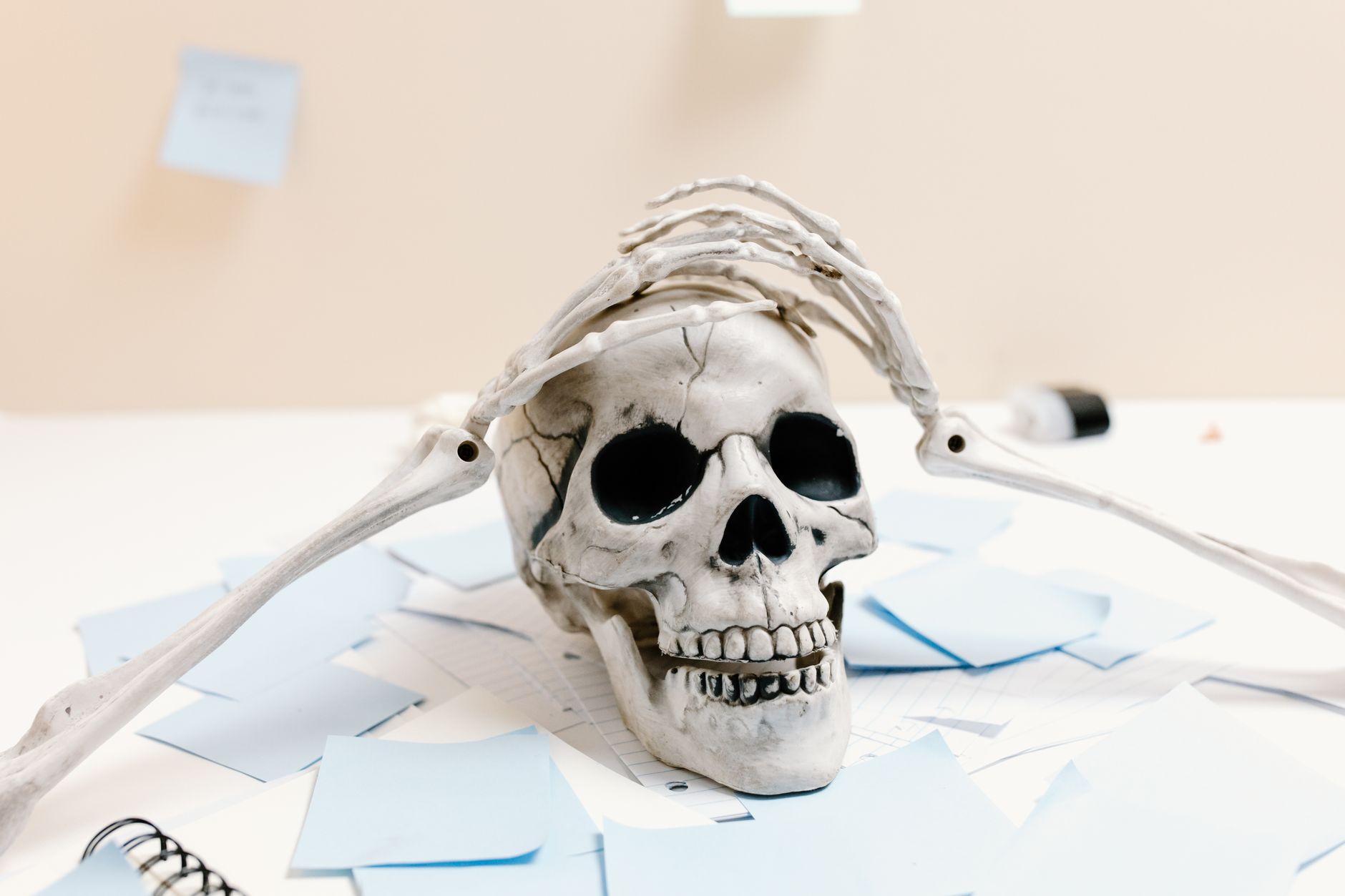 A skeleton rests on a desk with papers, symbolizing exhaustion and overwork.